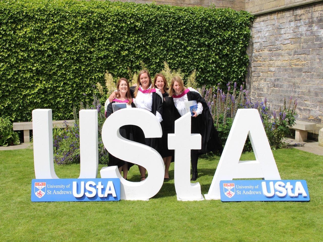 Four students standing behind the large UStA letters at Graduation.